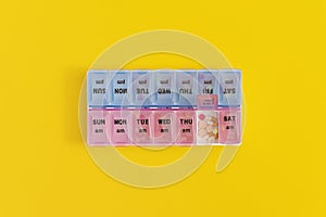 Daily pill box with medical pills on yellow background