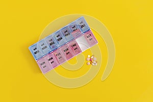 Daily pill box with medical pills on yellow background