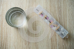 Pill box with pills and capsule vitamins and glass of water