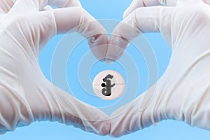 A pill with a riel currency sign inside a heart made from hands in medical gloves on a blue background. Rise in the price of