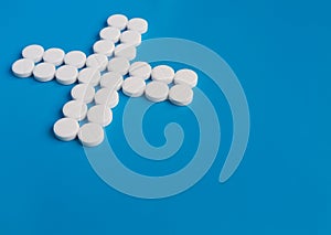 Pill white round medications laid out in the shape of a cross or X on a blue background