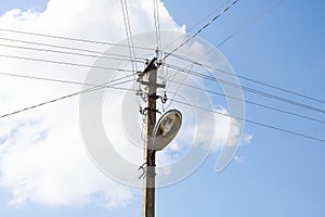 Pillar with lantern and electric wires against blue cloudy sky
