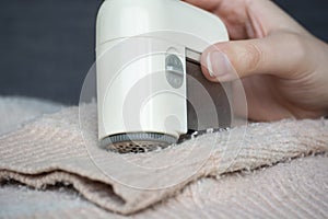 Pilled sweater. Woman hand using handheld electric fabric shaver fuzz remover device machine for removing fuzz, lint and pills