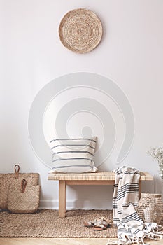 Pillow and blanket on wooden stool in white living room interior with brown plate. Real photo