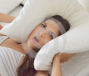 Pillow ears. Woman covering ears with pillow because of noise.