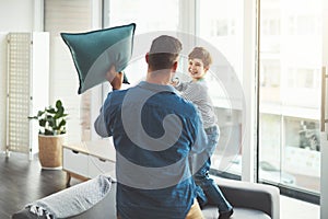Pillow fight. a cheerful little boy and his father having a pillow fight together in the living room at home during the
