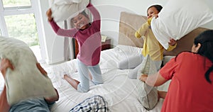 Pillow fight, excited and parents with their girl children on bed being playful and having fun together. Happy, smile