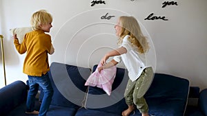 Pillow fight. Mischievous preschooler children jumping on a sofa and hitting each other with pillows. Boy and girl play together.