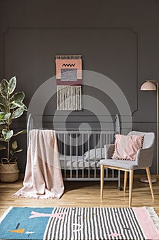 Pillow on grey armchair next to bed with blanket in child`s bedr