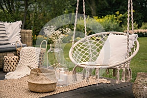Pillow on hanging chair and basket on carpet in the garden during spring