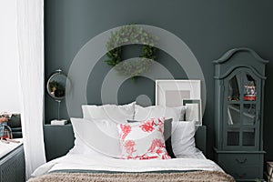 Pillows on the bed, above which a Christmas wreath hangs on a dark wall. Chest of drawers, mirror and mockups photo frames