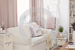 Pillows and blanket on white sofa in pink living room interior with drapes and flowers. Real photo