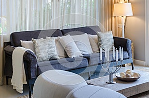 Pillows on blue sofa with lamp and candleholders on wooden table