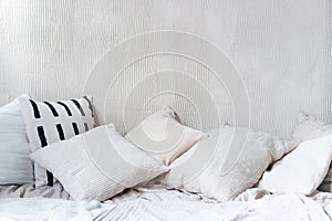 Pillows and cushions on crumpled bed against textured wall