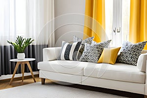 Pillows with geometric pattern lying on a white sofa in cozy living room with yellow curtains