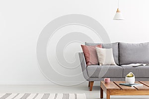 Pillows on grey settee and wooden table with copy space on the wall. Real photo