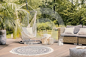 Pillows on hammock on terrace with round rug and rattan sofa in photo