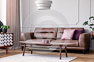 Pillows on leather couch in retro living room interior with lamp above wooden table. Real photo