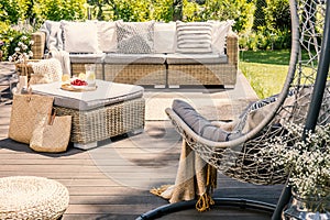 Pillows on rattan couch near table on patio with hanging chair in the garden. Real photo