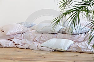 Pillows in soft maroon and green, rumpled beige blanket on large bed.