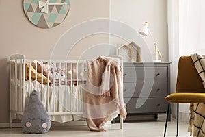 Pillows and toy in white wooden crib with pastel pink blanket in bright nursery