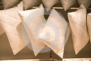 Pillows of white color suspended on a crossbeam in rows. Household items, light industry