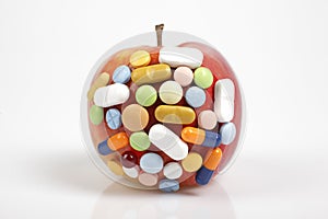 Pills on apple on white background symbolizing chemical contamination of food