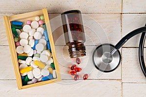 Pills in botle and wooden box with stethoscope and heart on white wooden table. Medical concept. Top views with clear space