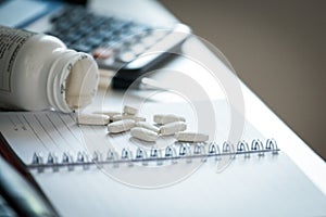 Pills and bottle on notebook in office desk