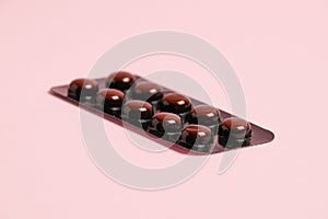 Pills in brown blister pack on pink paper background with copy space.