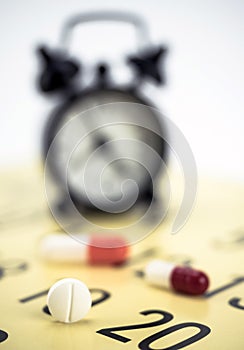 Pills on a calendar next to a clock