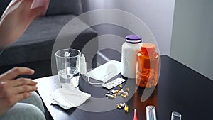 Pills, capsules and thermometer on the table. Woman taking medication.