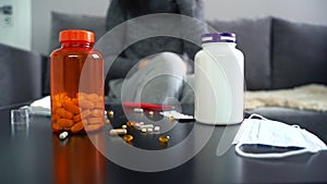 Pills, capsules and thermometer on the table. Woman taking medication.