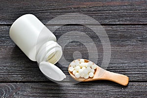 Pills and capsules in wooden spoons on wooden background. Homeopathic globules. Copy space. Vitamins, prebiotics, probiotics. Heal photo
