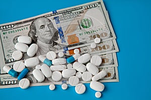 Pills on dollar money on blue background. Medicine expenses. High costs of medication concept. Close up