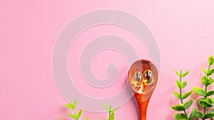 Pills of fish oil as a dietary supplement lies on a wooden spoon with an isolated pink background