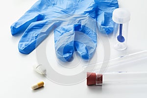 Pills, glass tubes, stool test sampler and blue latex glove on white