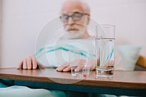 Pills and glass of water in front of senior man