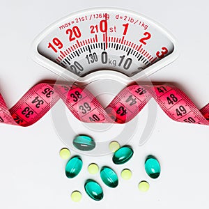 Pills with measuring tape on white scales