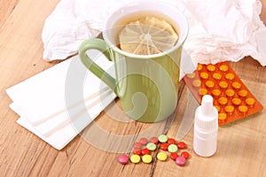 Pills and nose drops for colds, handkerchiefs and hot tea with lemon