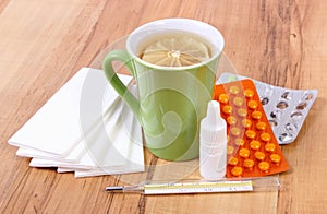 Pills and nose drops for colds, handkerchiefs and hot tea with lemon