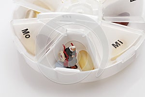 Pills and pensioner figurine in pill organiser, close up
