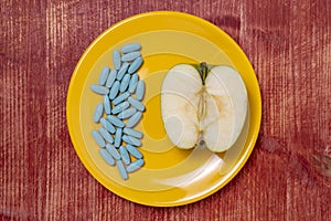 Pills in a plate with an apple half on a wooden table