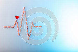 Pills in shape of cardiogram pulse on blue gradient background. Vitamins and red glass heart, symbol of healthy lifestyle.