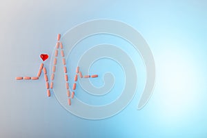 Pills in shape of cardiogram pulse on blue gradient background. Vitamins and red glass heart, symbol of healthy lifestyle.