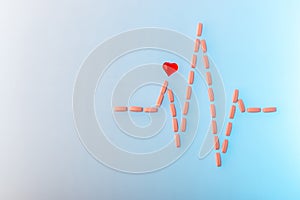 Pills in shape of cardiogram pulse on blue gradient background. Vitamins and red glass heart, symbol of healthy lifestyle.