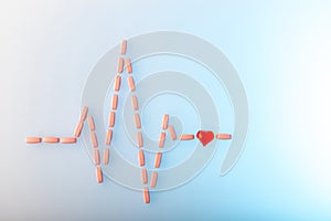 Pills in shape of cardiogram pulse on blue gradient background. Vitamins and red glass heart, symbol of healthy lifestyle.