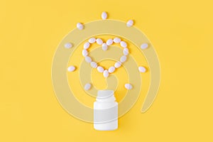 Pills in shape of heart dropped from bottle on yellow background. Flat lay, top view