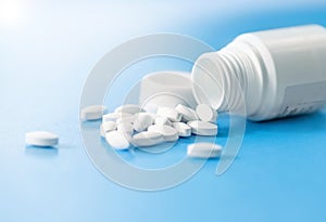 Pills spilled out of white bottle on light blue background with copy space. Medical healthcare concept