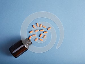 Pills spilling from a amber bottle, on blue paper background. op view